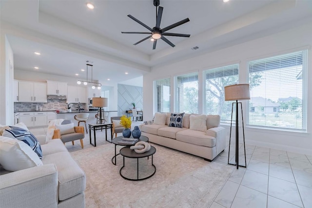 living area featuring a tray ceiling, a ceiling fan, recessed lighting, and light marble finish flooring