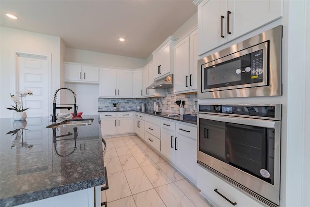 kitchen featuring stainless steel appliances, a sink, light marble finish flooring, under cabinet range hood, and white cabinetry