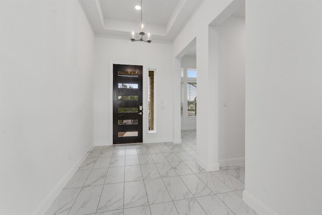 entryway featuring light marble finish floors, a chandelier, a tray ceiling, and baseboards