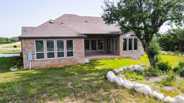 rear view of house featuring brick siding, a patio, a yard, and roof with shingles