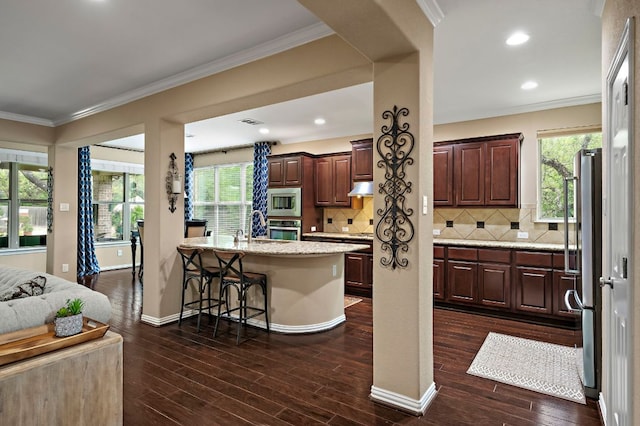 1720 Foxboro Ln, Cedar Park, TX 78613 - kitchen featuring appliances with stainless steel finishes, under cabinet range hood, dark wood-type flooring, a breakfast bar, and decorative backsplash