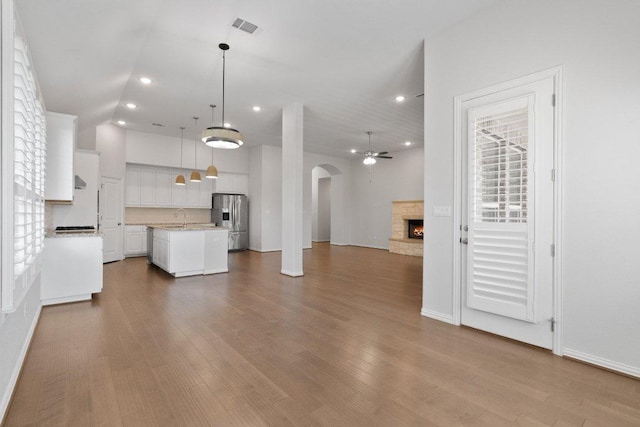unfurnished living room with a stone fireplace, a sink, arched walkways, dark wood-style flooring, and recessed lighting
