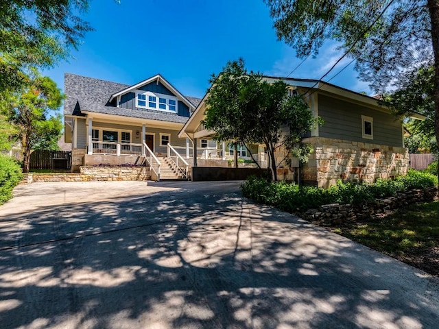 view of front of home featuring covered porch, stone siding, fence, and board and batten siding