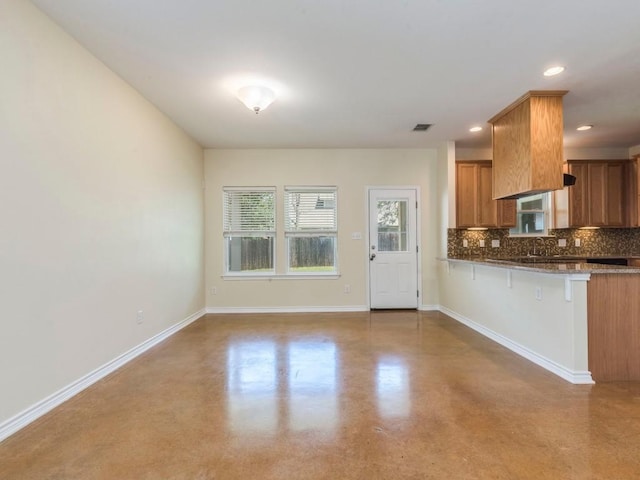 kitchen featuring brown cabinets, tasteful backsplash, concrete floors, baseboards, and recessed lighting