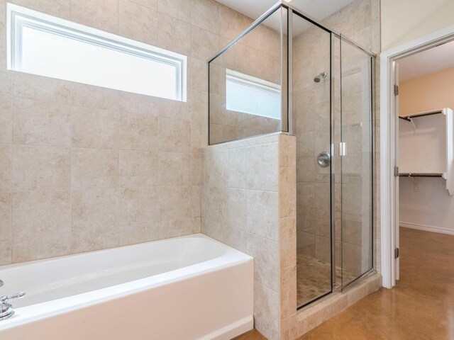 full bathroom featuring a shower stall, a spacious closet, a garden tub, and finished concrete flooring