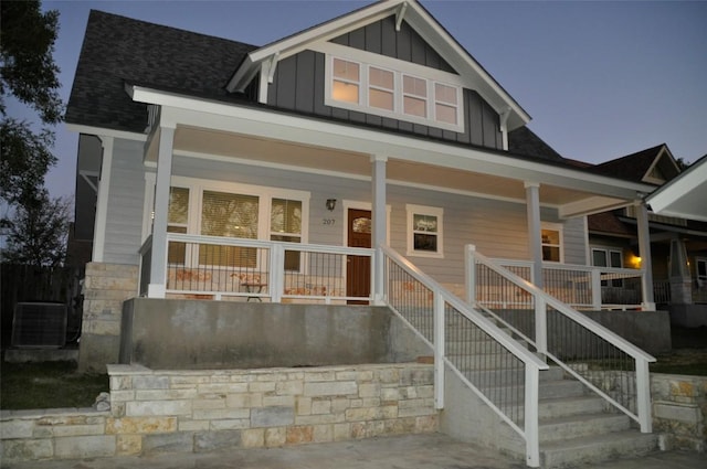 view of front of home with covered porch, board and batten siding, central air condition unit, and stone siding