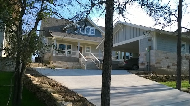 view of front of home featuring board and batten siding, covered porch, concrete driveway, and stone siding