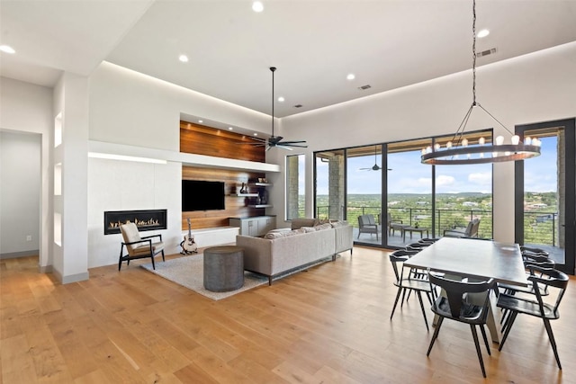 living room featuring a lit fireplace, recessed lighting, light wood-type flooring, a ceiling fan, and a chandelier