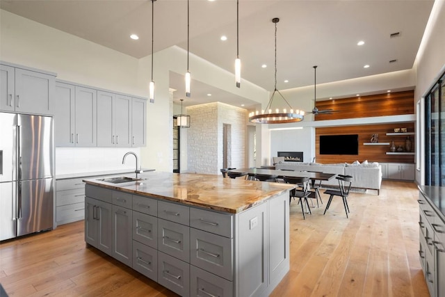 kitchen with stainless steel refrigerator, gray cabinets, a sink, a chandelier, and light stone countertops