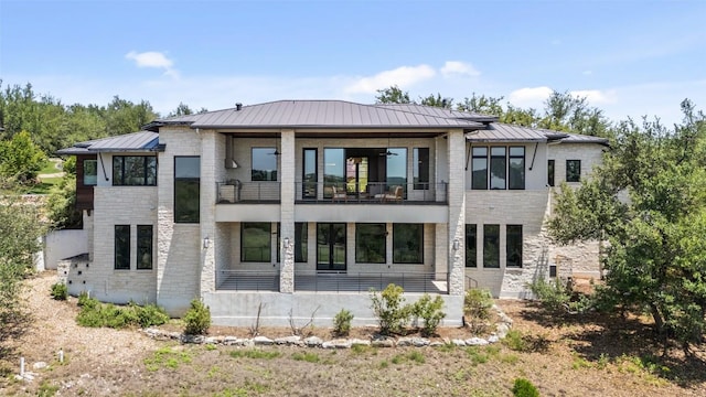 rear view of house featuring a balcony, a standing seam roof, metal roof, and brick siding