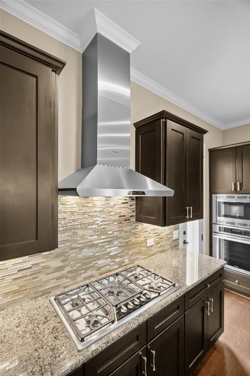 1044 Highknoll Ln, Georgetown, TX 78628 - kitchen featuring stainless steel appliances, wall chimney range hood, dark brown cabinetry, crown molding, and tasteful backsplash
