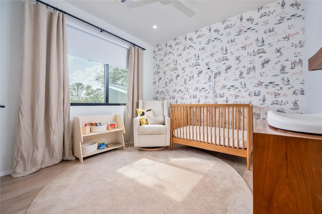 bedroom featuring a crib, wood finished floors, recessed lighting, and a ceiling fan