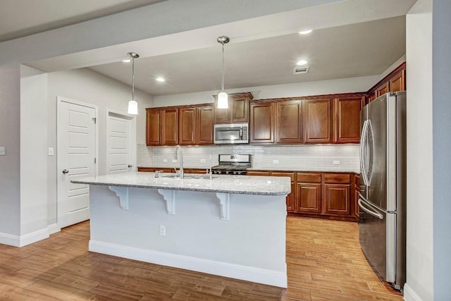 kitchen with stainless steel appliances, a sink, a breakfast bar, light stone counters, and decorative backsplash