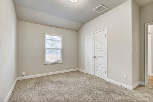 unfurnished bedroom featuring light colored carpet, vaulted ceiling, a closet, and baseboards