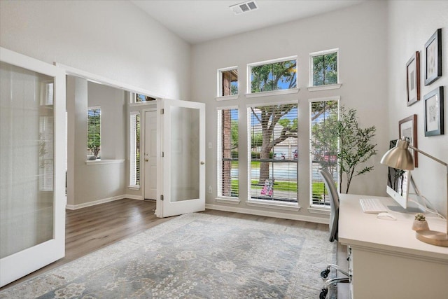 office featuring french doors, wood finished floors, plenty of natural light, and a towering ceiling