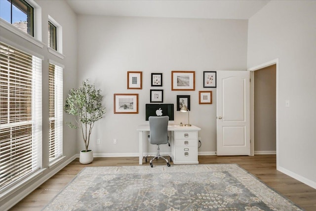 office space with a high ceiling, wood finished floors, healthy amount of natural light, and baseboards
