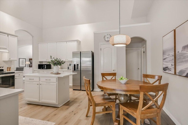 dining space with arched walkways, light wood-style floors, a towering ceiling, and baseboards