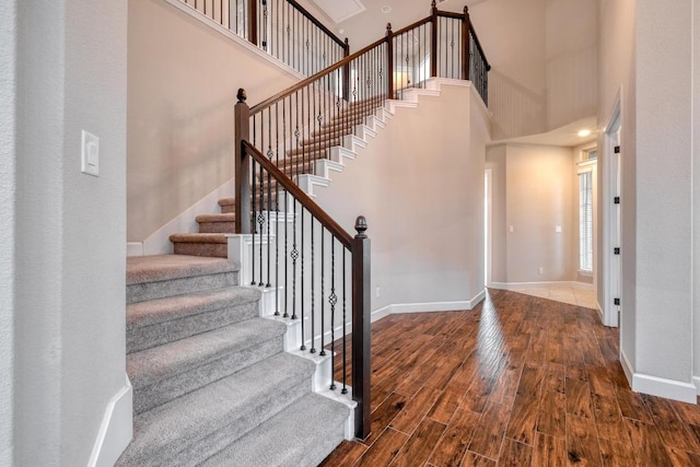 stairs featuring wood finished floors, baseboards, and a high ceiling