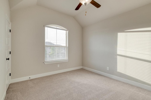 carpeted spare room featuring a ceiling fan, vaulted ceiling, and baseboards