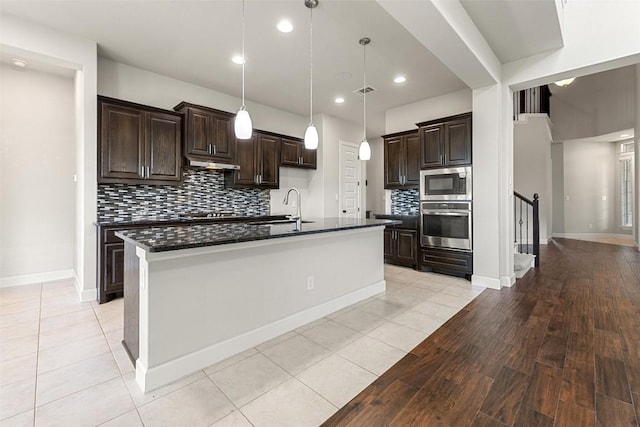 3351 Vasquez Pl, Round Rock, TX 78665 - kitchen with stainless steel appliances, under cabinet range hood, dark brown cabinetry, backsplash, and a center island with sink