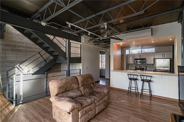 living area with wood finished floors, an AC wall unit, and baseboards