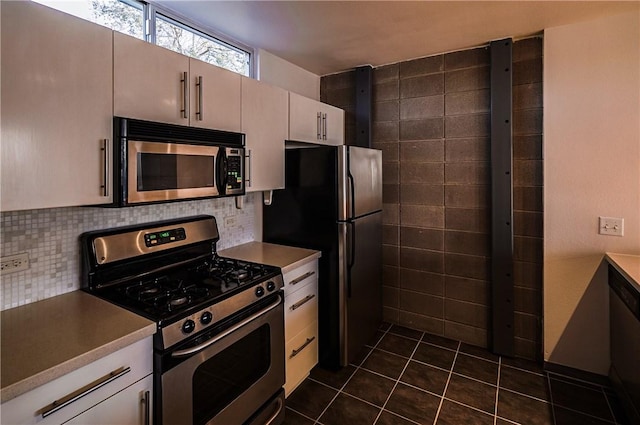kitchen with appliances with stainless steel finishes, tasteful backsplash, dark tile patterned floors, and light countertops
