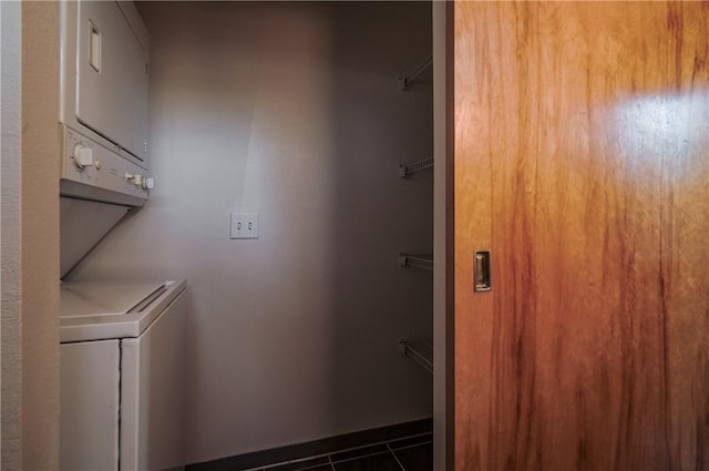 washroom with stacked washing machine and dryer, dark tile patterned floors, and baseboards