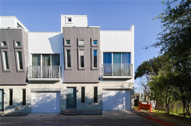 rear view of property with an attached garage, a balcony, and stucco siding