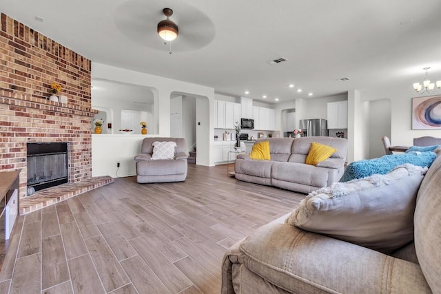 282 Crimson Ln, Kyle, TX 78640 - living room with a ceiling fan, light wood-type flooring, arched walkways, a fireplace, and a chandelier