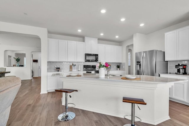282 Crimson Ln, Kyle, TX 78640 - kitchen with black appliances, arched walkways, a kitchen bar, decorative backsplash, and light countertops