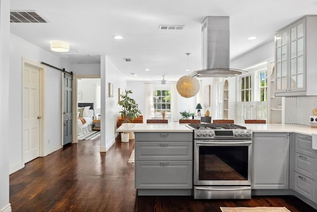 kitchen featuring gray cabinets, stainless steel range with gas stovetop, island exhaust hood, a peninsula, and light countertops