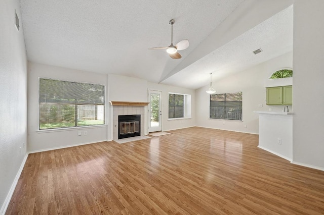unfurnished living room featuring a ceiling fan, lofted ceiling, a textured ceiling, healthy amount of natural light, and a fireplace