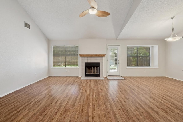 unfurnished living room featuring lofted ceiling, healthy amount of natural light, light wood finished floors, ceiling fan, and a tile fireplace