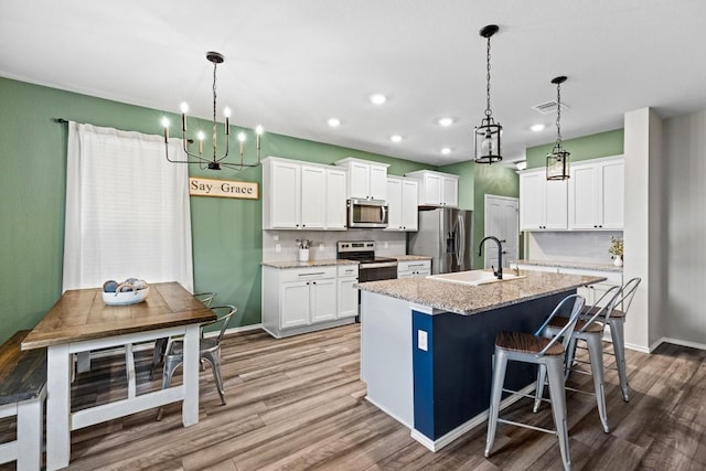 109 Reagor Dr, Taylor, TX 76574 - kitchen with appliances with stainless steel finishes, a chandelier, an island with sink, wood finished floors, and recessed lighting