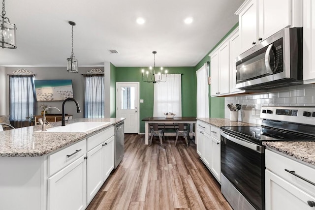 109 Reagor Dr, Taylor, TX 76574 - kitchen with stainless steel appliances, a chandelier, wood finished floors, white cabinetry, and tasteful backsplash