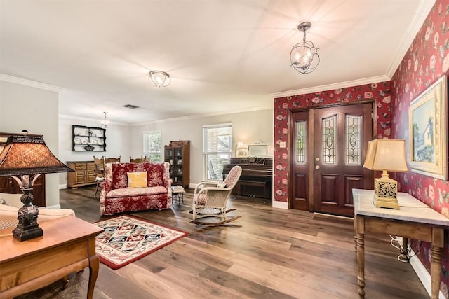 living area with a chandelier, wallpapered walls, crown molding, wood finished floors, and baseboards