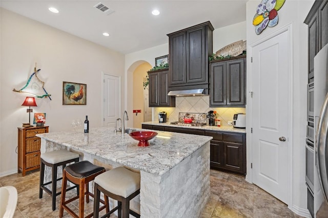 4216 Hannover Way, Round Rock, TX 78681 - kitchen with backsplash, arched walkways, under cabinet range hood, a kitchen island with sink, and recessed lighting