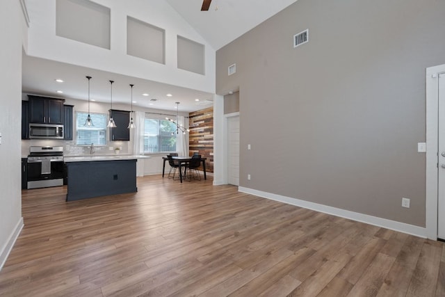 kitchen with appliances with stainless steel finishes, light countertops, light wood finished floors, a center island, and decorative backsplash