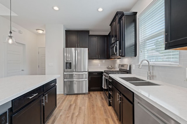kitchen with appliances with stainless steel finishes, a sink, light wood finished floors, tasteful backsplash, and decorative light fixtures