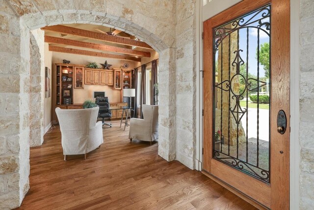 foyer featuring arched walkways, wood finished floors, plenty of natural light, and beam ceiling