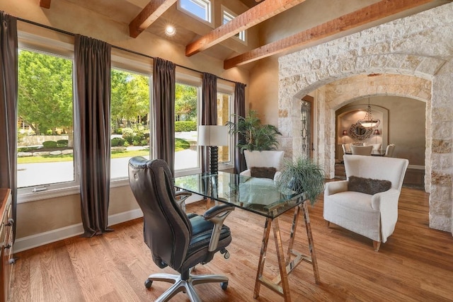 office featuring plenty of natural light, beamed ceiling, wood finished floors, arched walkways, and baseboards