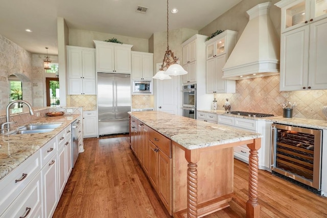 kitchen featuring wine cooler, built in appliances, a sink, premium range hood, and light wood finished floors