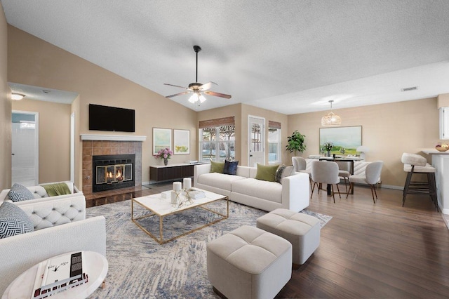 living area featuring dark wood finished floors, a textured ceiling, a tiled fireplace, baseboards, and lofted ceiling