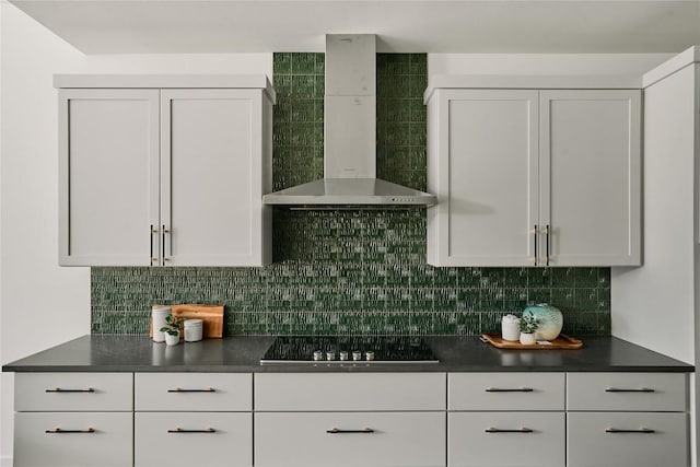 kitchen with wall chimney range hood, black electric cooktop, dark countertops, white cabinets, and backsplash