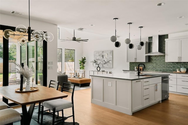 kitchen with wall chimney range hood, a sink, decorative backsplash, dishwasher, and light wood-style floors