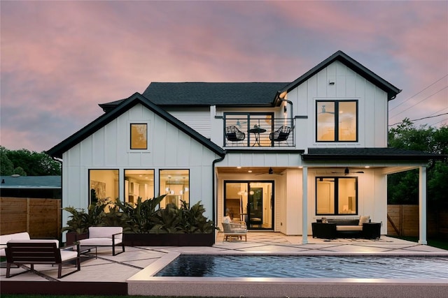 back of property at dusk with a balcony, outdoor lounge area, ceiling fan, and a patio area