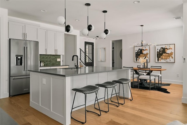 kitchen featuring high end fridge, a sink, dark countertops, a kitchen breakfast bar, and light wood-style floors