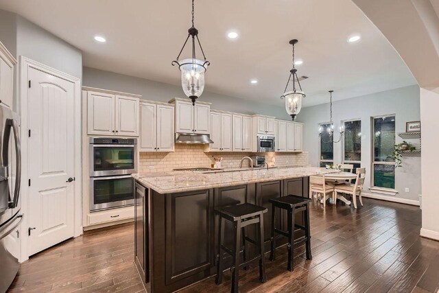 2516 Arion Cir, Austin, TX 78730 - kitchen featuring appliances with stainless steel finishes, under cabinet range hood, decorative backsplash, light stone countertops, and dark wood-style flooring