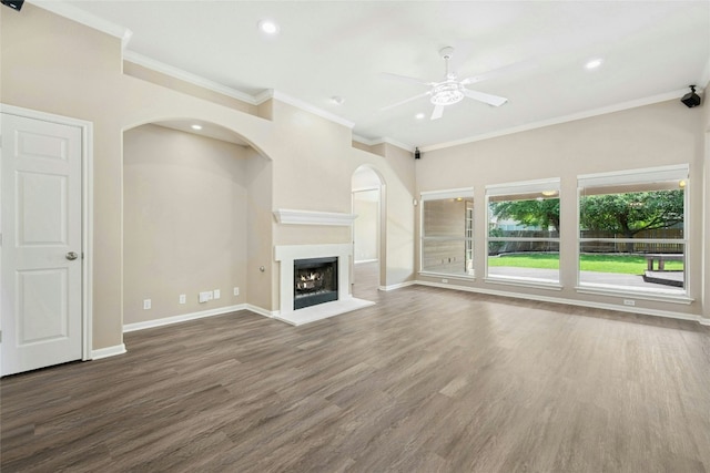 unfurnished living room with ceiling fan, baseboards, wood finished floors, a warm lit fireplace, and crown molding