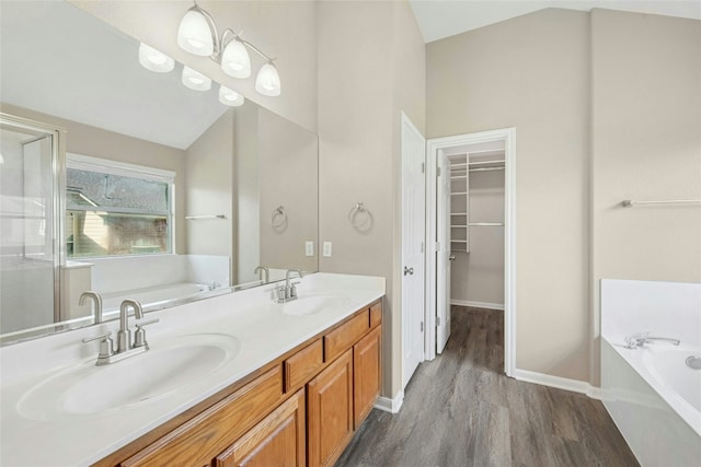 full bathroom with wood finished floors, a bath, a walk in closet, lofted ceiling, and baseboards